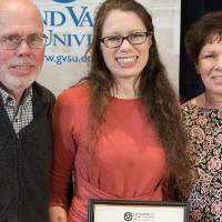 Photo of graduate student holding her award with her parents on either side of her